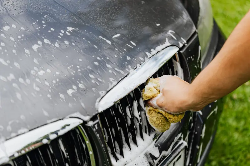 Detailed view of a hand washing a car grille with a soapy sponge outdoors