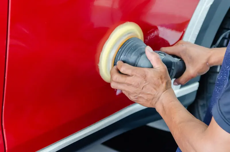 Close-up of a worker buffing red car paint for shine and maintenance