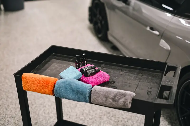 Colorful towels and detailing products on a cart beside a car in a garage