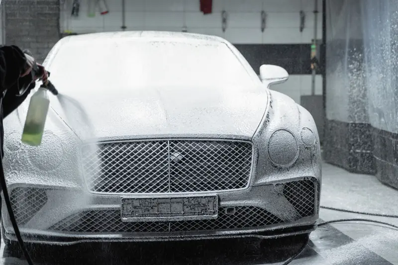 A luxury car is covered in foam during a detailed wash inside a garage