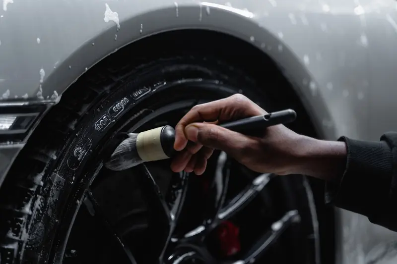 Detailed shot of a hand using a brush to clean a car tire and wheel during a wash